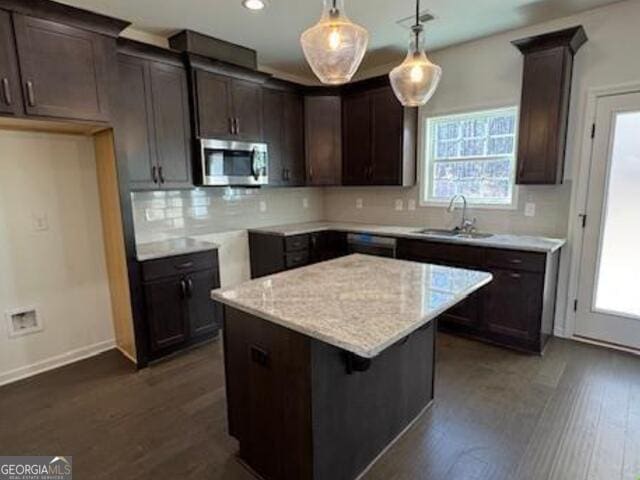 kitchen featuring hanging light fixtures, dark hardwood / wood-style flooring, a center island, sink, and light stone counters