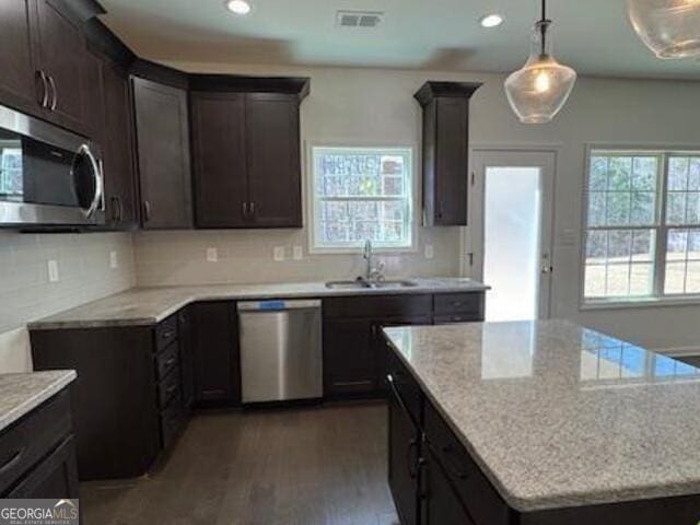 kitchen with appliances with stainless steel finishes, hardwood / wood-style flooring, hanging light fixtures, light stone countertops, and sink