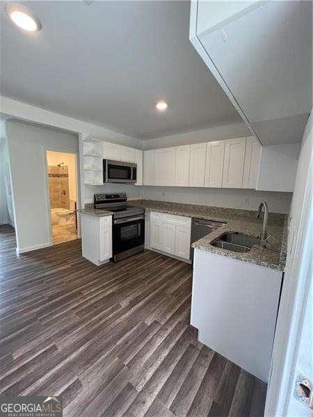 kitchen with sink, white cabinetry, stainless steel appliances, dark hardwood / wood-style floors, and stone countertops