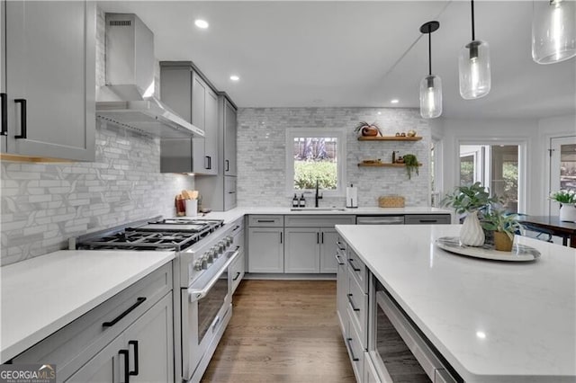 kitchen with wall chimney exhaust hood, wood finished floors, gray cabinets, stainless steel stove, and a sink