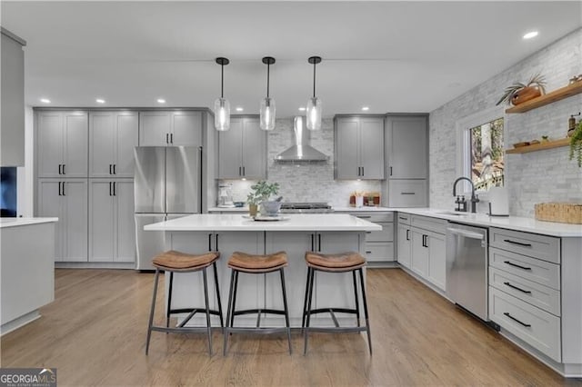 kitchen featuring stainless steel appliances, gray cabinets, light wood-style floors, and wall chimney exhaust hood