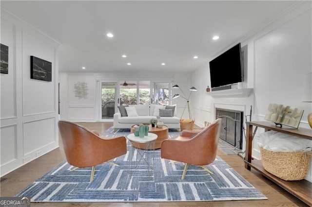 living room with a fireplace with raised hearth, recessed lighting, wood finished floors, and a decorative wall