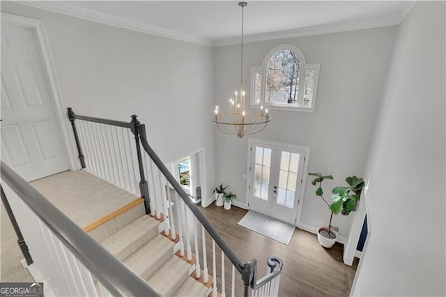 entryway featuring french doors, crown molding, an inviting chandelier, wood finished floors, and stairs