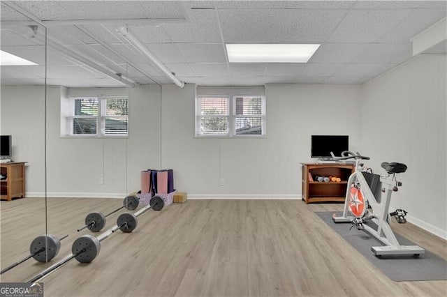 exercise room featuring baseboards, wood finished floors, a paneled ceiling, and a healthy amount of sunlight