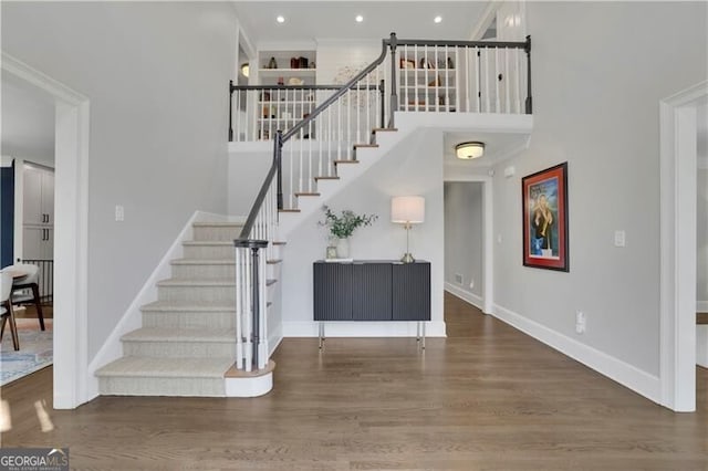 stairway with a towering ceiling, baseboards, and wood finished floors