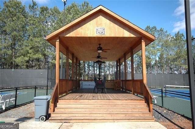 deck featuring a tennis court, fence, and a ceiling fan