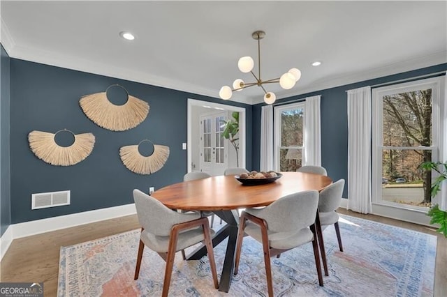 dining space with wood finished floors, visible vents, baseboards, ornamental molding, and an inviting chandelier