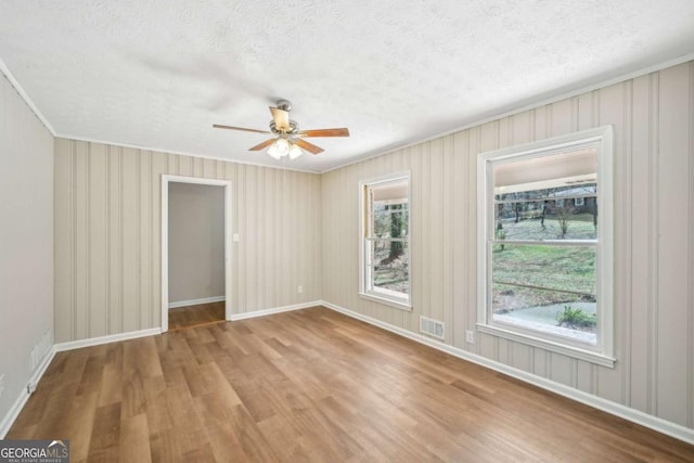 empty room with ceiling fan, ornamental molding, a textured ceiling, and light wood-type flooring