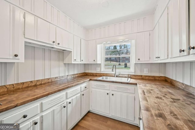 kitchen featuring white cabinetry, sink, wood counters, and light hardwood / wood-style floors