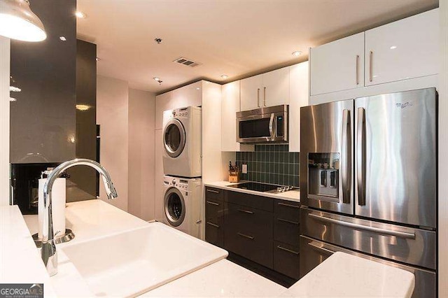 kitchen featuring stacked washer and clothes dryer, appliances with stainless steel finishes, a sink, light countertops, and backsplash