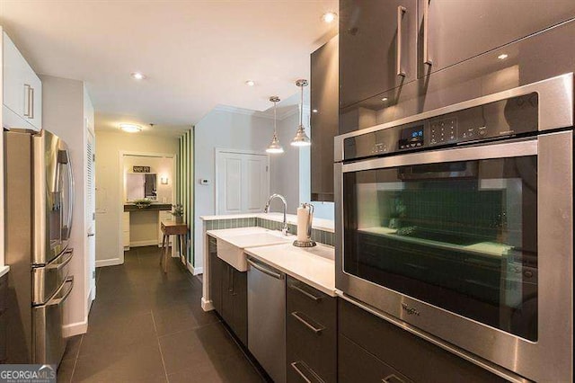 kitchen featuring dark brown cabinetry, appliances with stainless steel finishes, light countertops, pendant lighting, and a sink