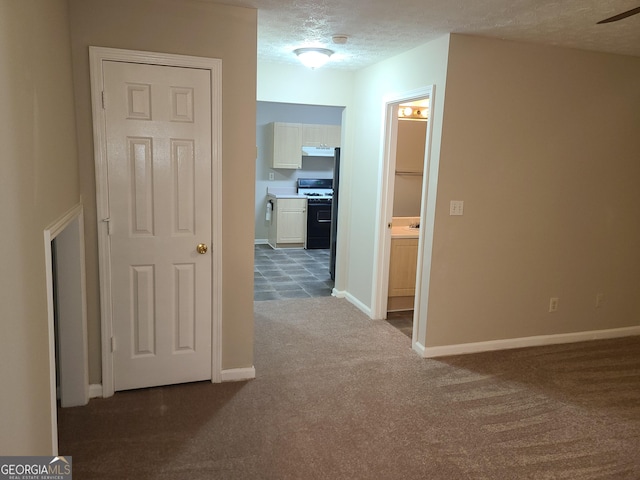 hall featuring a textured ceiling and dark colored carpet