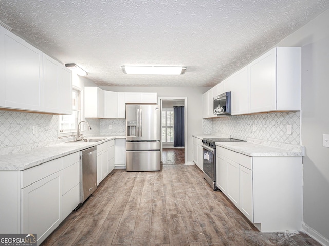 kitchen featuring sink, light wood-type flooring, appliances with stainless steel finishes, decorative backsplash, and white cabinets