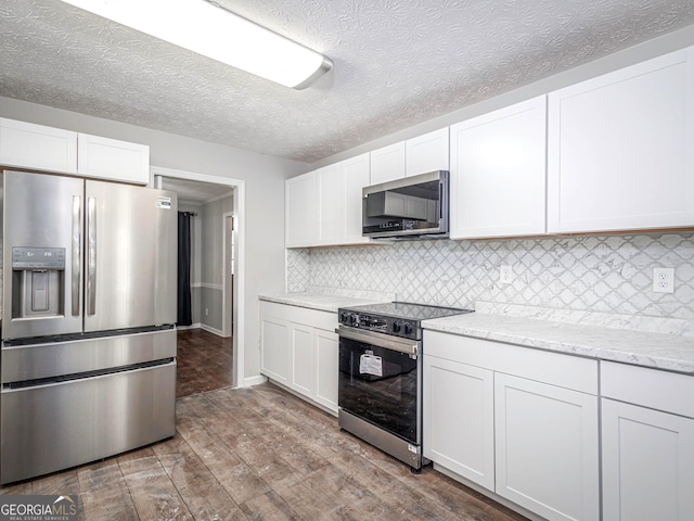 kitchen featuring light wood-type flooring, appliances with stainless steel finishes, white cabinets, light stone countertops, and backsplash