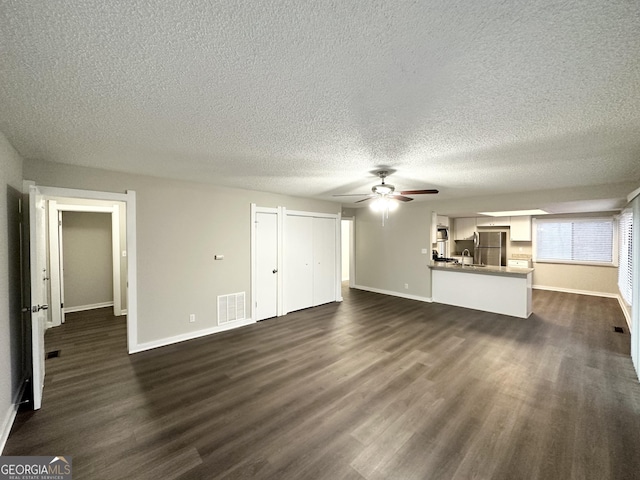 unfurnished living room with a textured ceiling, dark wood-type flooring, and ceiling fan