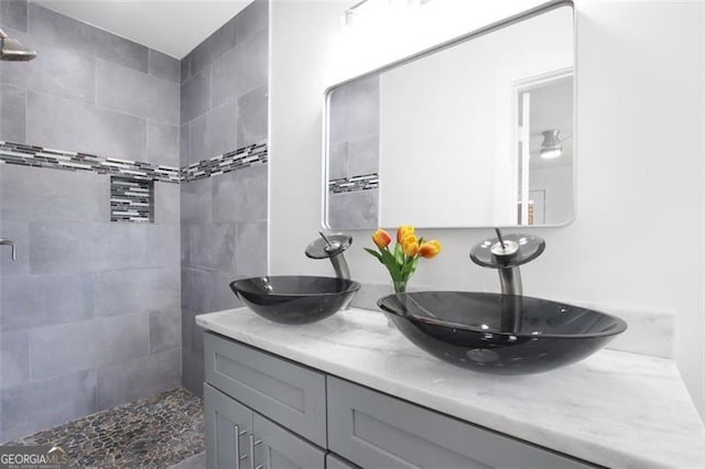 full bathroom featuring a tile shower, double vanity, and a sink