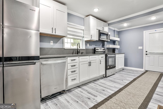 kitchen featuring appliances with stainless steel finishes, light hardwood / wood-style floors, ornamental molding, sink, and white cabinetry