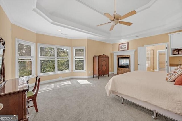 bedroom with a multi sided fireplace, a tray ceiling, light colored carpet, and crown molding