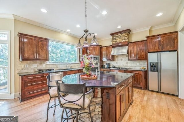 kitchen with appliances with stainless steel finishes, wall chimney range hood, pendant lighting, a kitchen island, and sink