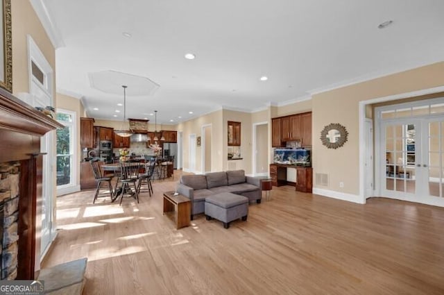 living room with light wood-type flooring, french doors, a stone fireplace, and ornamental molding