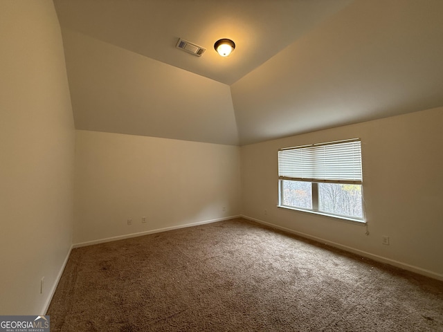 carpeted empty room with baseboards, visible vents, and vaulted ceiling