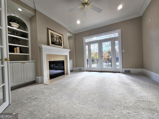 unfurnished living room with built in features, light colored carpet, a high end fireplace, crown molding, and french doors