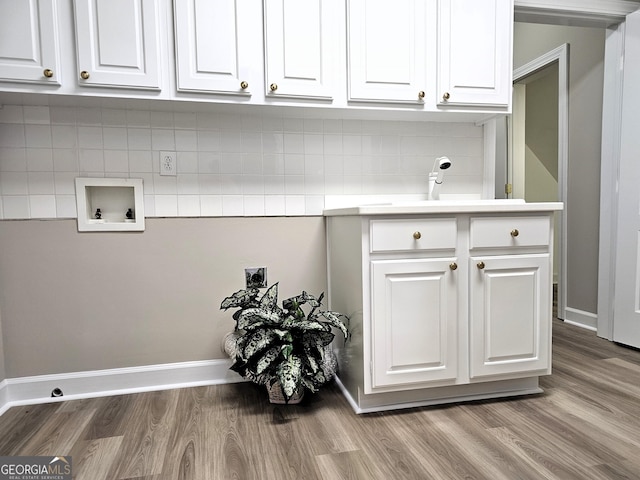 clothes washing area with hardwood / wood-style floors, hookup for a washing machine, and cabinets