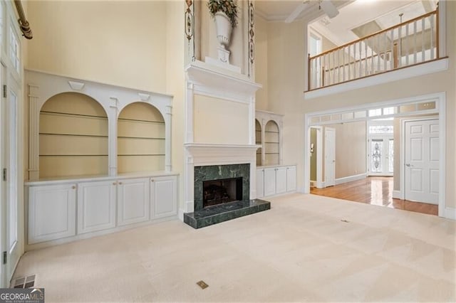 unfurnished living room with light carpet, crown molding, a fireplace, and built in features