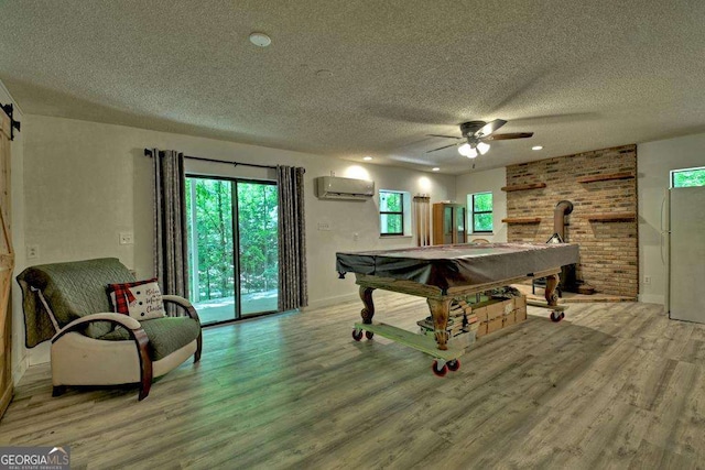 playroom with billiards, a textured ceiling, light wood-type flooring, an AC wall unit, and ceiling fan