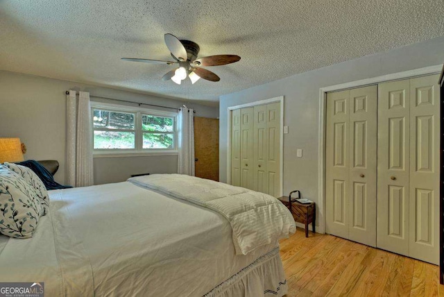 bedroom with multiple closets, ceiling fan, light hardwood / wood-style flooring, and a textured ceiling