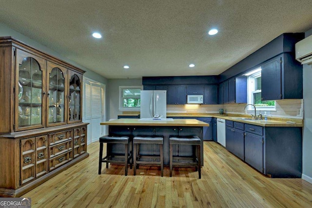 kitchen featuring sink, a center island, light wood-type flooring, a kitchen breakfast bar, and white appliances