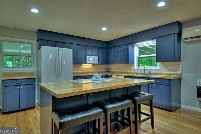 kitchen with sink, a breakfast bar area, wooden counters, a center island, and white appliances