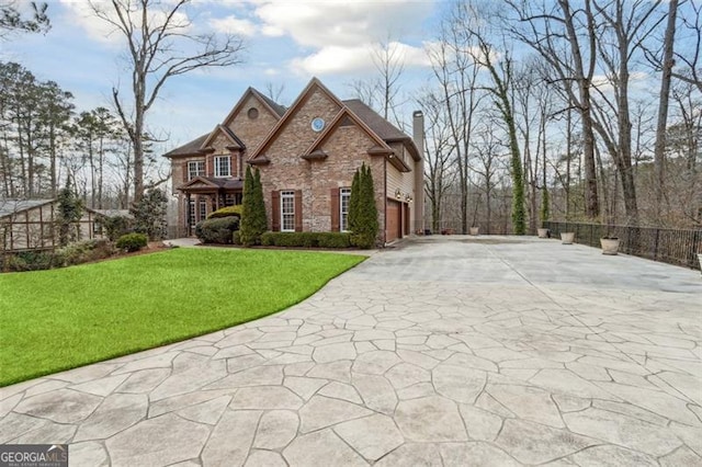 french provincial home featuring a chimney, stone siding, concrete driveway, and a front yard