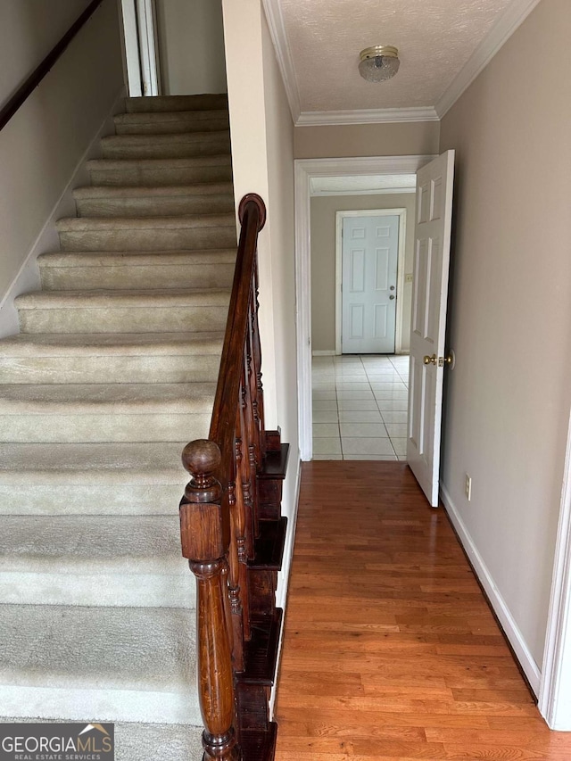 staircase with crown molding, wood-type flooring, and a textured ceiling