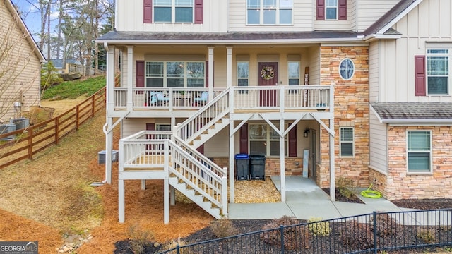 view of front of home featuring stone siding, stairway, roof with shingles, fence private yard, and board and batten siding