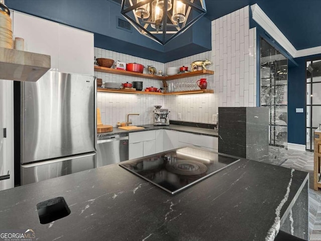 kitchen with tasteful backsplash, appliances with stainless steel finishes, white cabinets, and an inviting chandelier