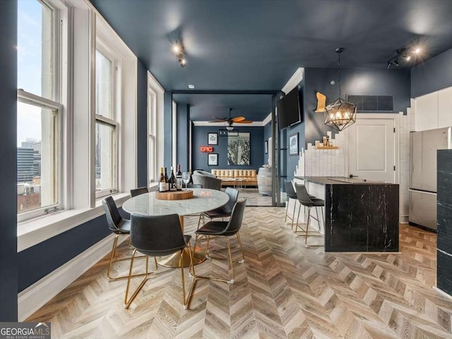 dining room with ceiling fan with notable chandelier, rail lighting, light parquet floors, and a high ceiling