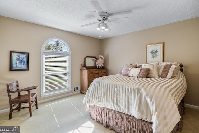 bedroom featuring a textured ceiling, light colored carpet, and ceiling fan