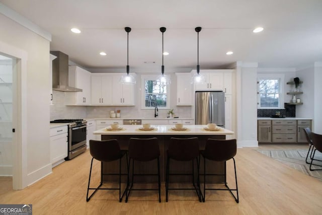 kitchen featuring stainless steel appliances, a kitchen island, wall chimney range hood, and white cabinets