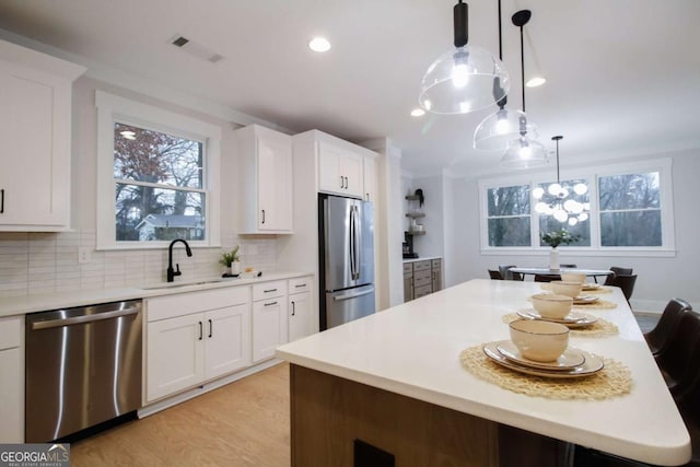 kitchen with appliances with stainless steel finishes, sink, hanging light fixtures, and white cabinets