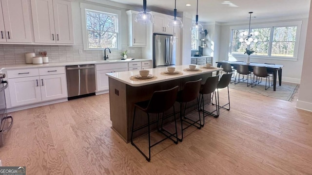 kitchen featuring a breakfast bar, a kitchen island, pendant lighting, stainless steel appliances, and white cabinets