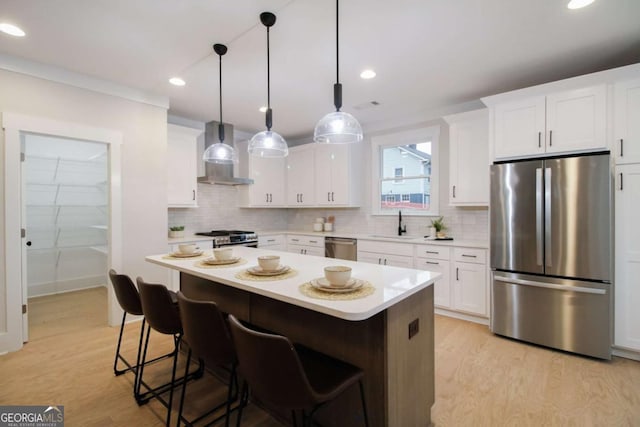 kitchen featuring wall chimney range hood, stainless steel appliances, white cabinets, and a kitchen island