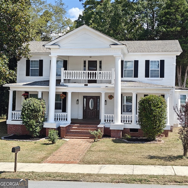 greek revival house with a balcony, a front yard, and covered porch