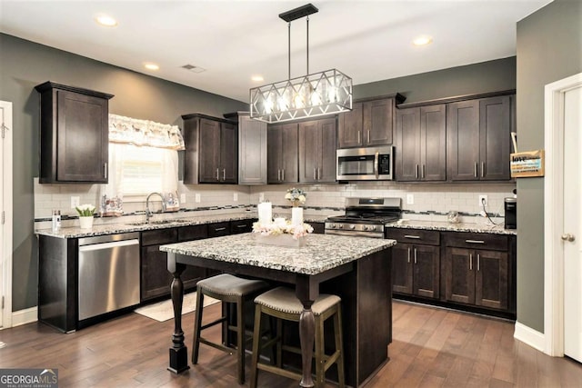 kitchen with dark brown cabinetry, sink, a center island, hanging light fixtures, and stainless steel appliances