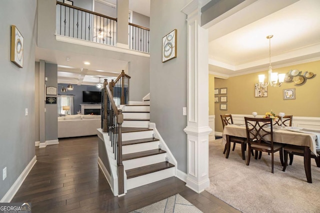 staircase with decorative columns, wood-type flooring, a notable chandelier, a raised ceiling, and crown molding