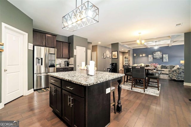 kitchen with stainless steel refrigerator with ice dispenser, a breakfast bar area, a center island, dark brown cabinets, and hanging light fixtures