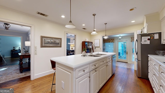 kitchen featuring sink, appliances with stainless steel finishes, white cabinetry, hanging light fixtures, and a center island with sink