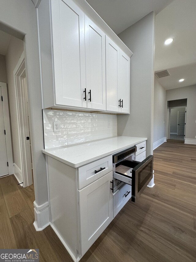 kitchen with light countertops, dark wood-type flooring, wall oven, and white cabinets