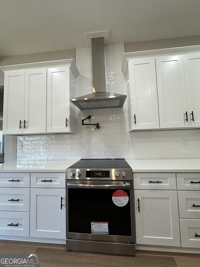 kitchen featuring wall chimney exhaust hood, wood finished floors, a kitchen island with sink, white cabinetry, and pendant lighting