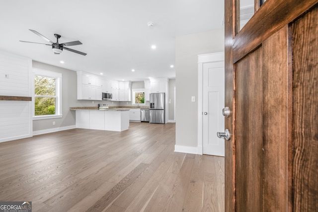 kitchen with white cabinetry, kitchen peninsula, hardwood / wood-style flooring, ceiling fan, and stainless steel appliances